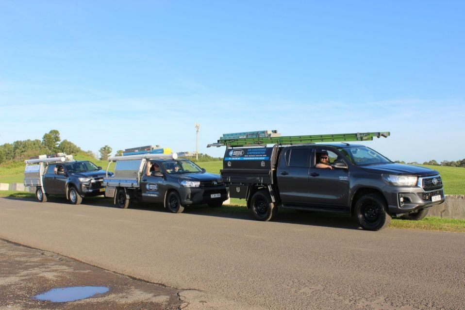 Three work trucks in a row on a road with men in the drivers seats