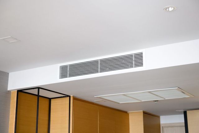 Ceiling-mounted air conditioning unit, white, gridded vent in a white ceiling.