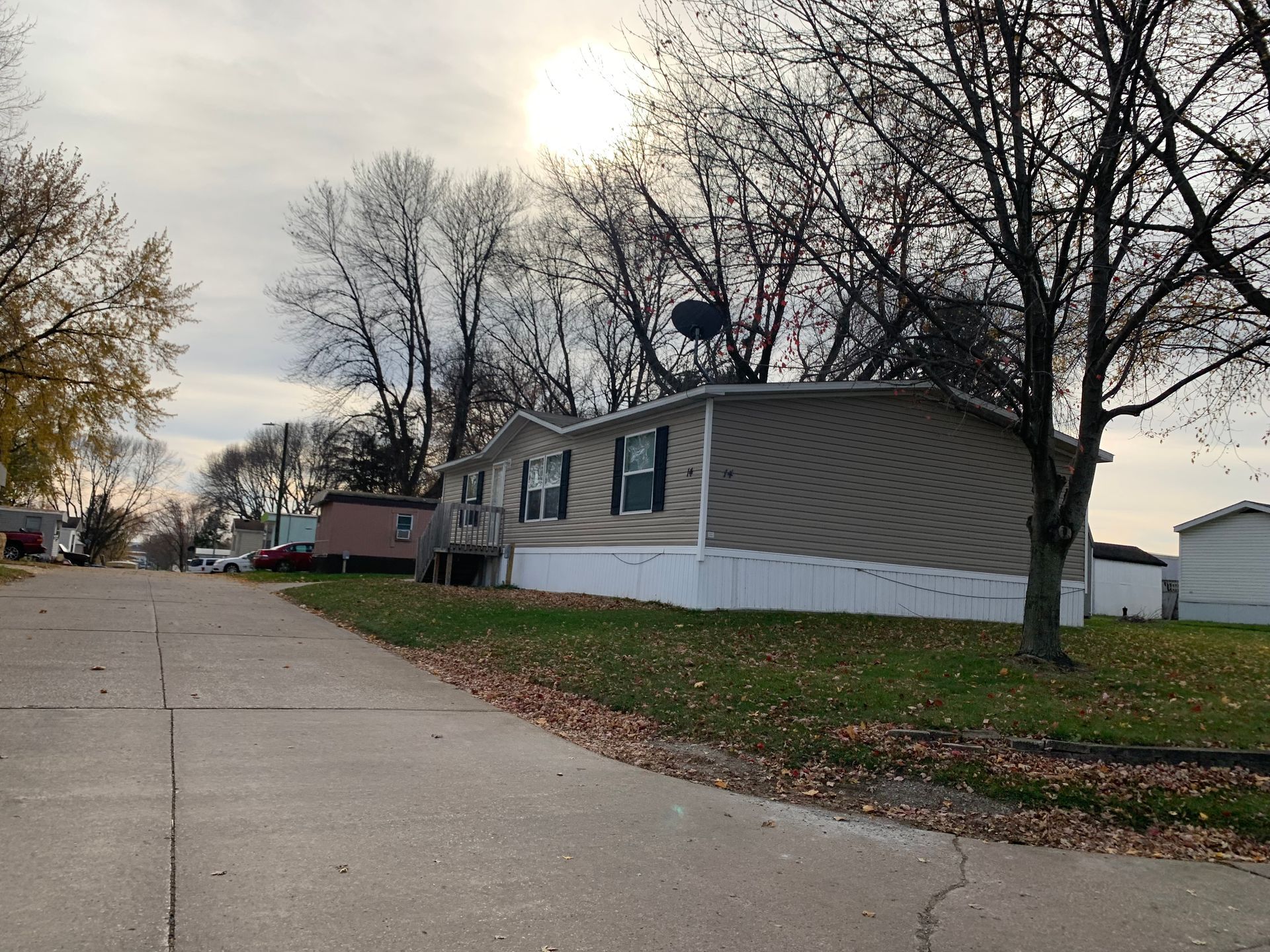 Suburban street with a beige mobile home, leafless trees, and a cloudy sky