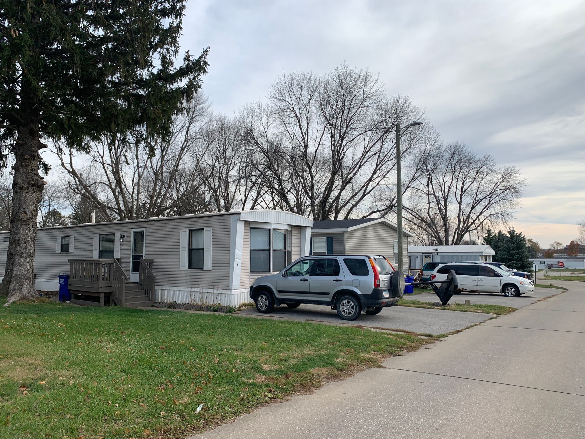 Mobile home on a quiet street with two parked SUVs under cloudy skies.