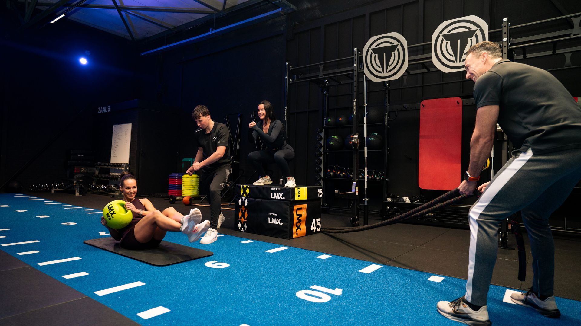 Twee mensen hurken op houten kisten in een sportschool, 