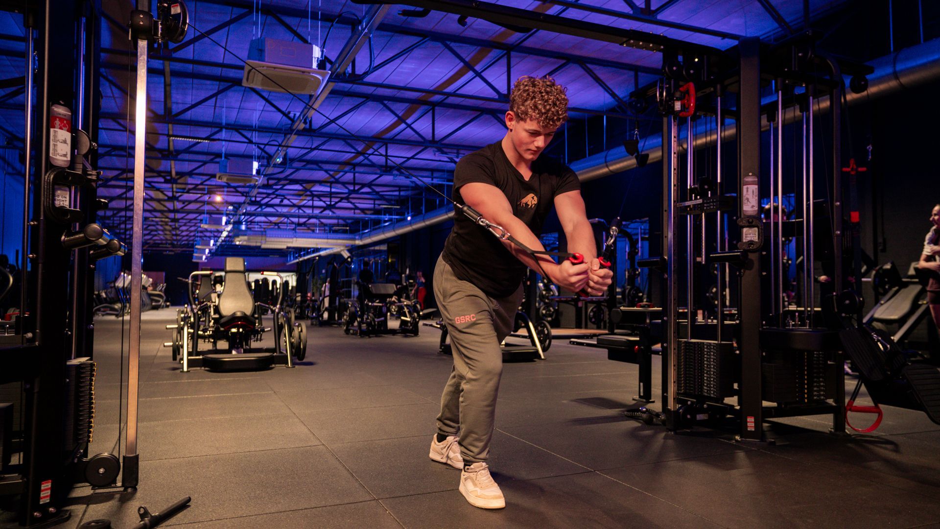 Man rent op een loopband in een sportschool, naast andere loopbanden bij grote ramen.