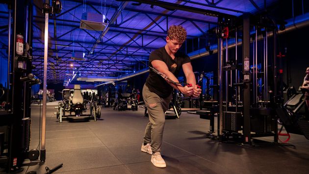 Man rent op een loopband in een sportschool, naast andere loopbanden bij grote ramen.