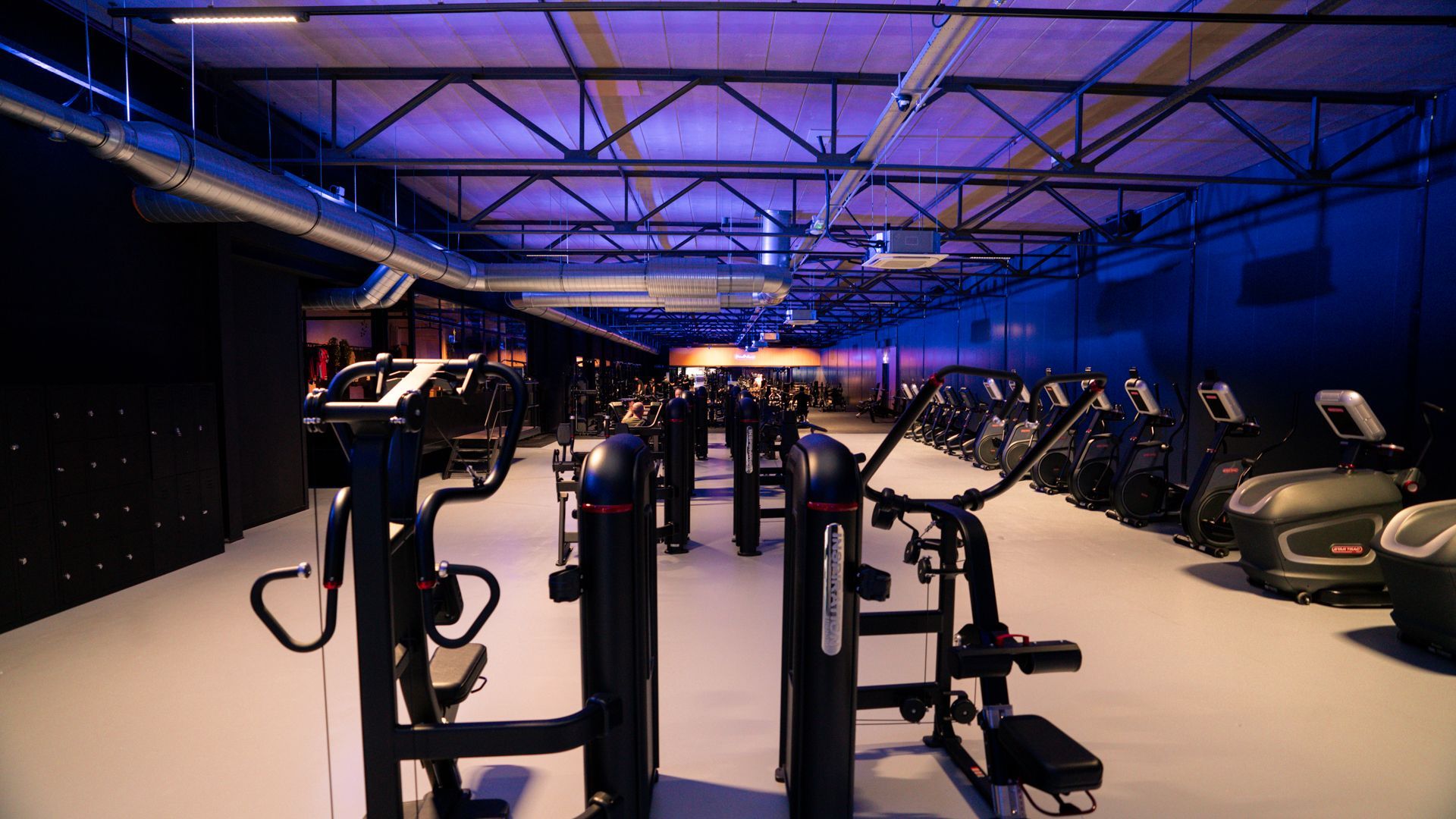 Interieur van een sportschool met loopbanden, halterbanken en gewichten bij de ramen.