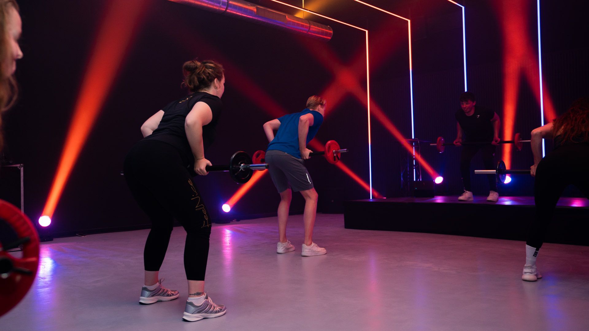 Mensen trainen met weerstandsbanden in een sportschool. Armen omhoog, geconcentreerde gezichtsuitdrukkingen.