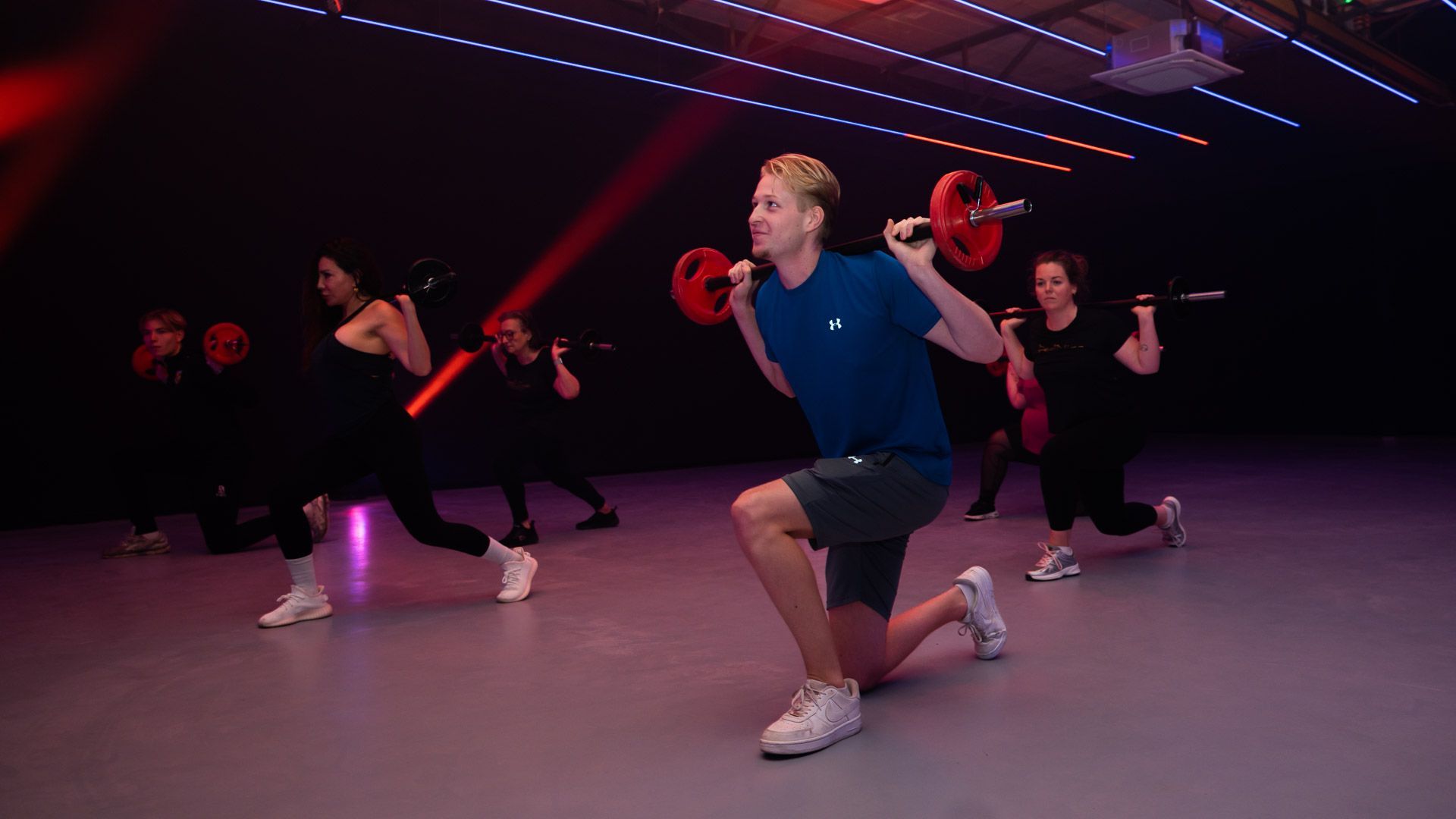 Man rent op een loopband in een sportschool, naast andere loopbanden bij grote ramen.