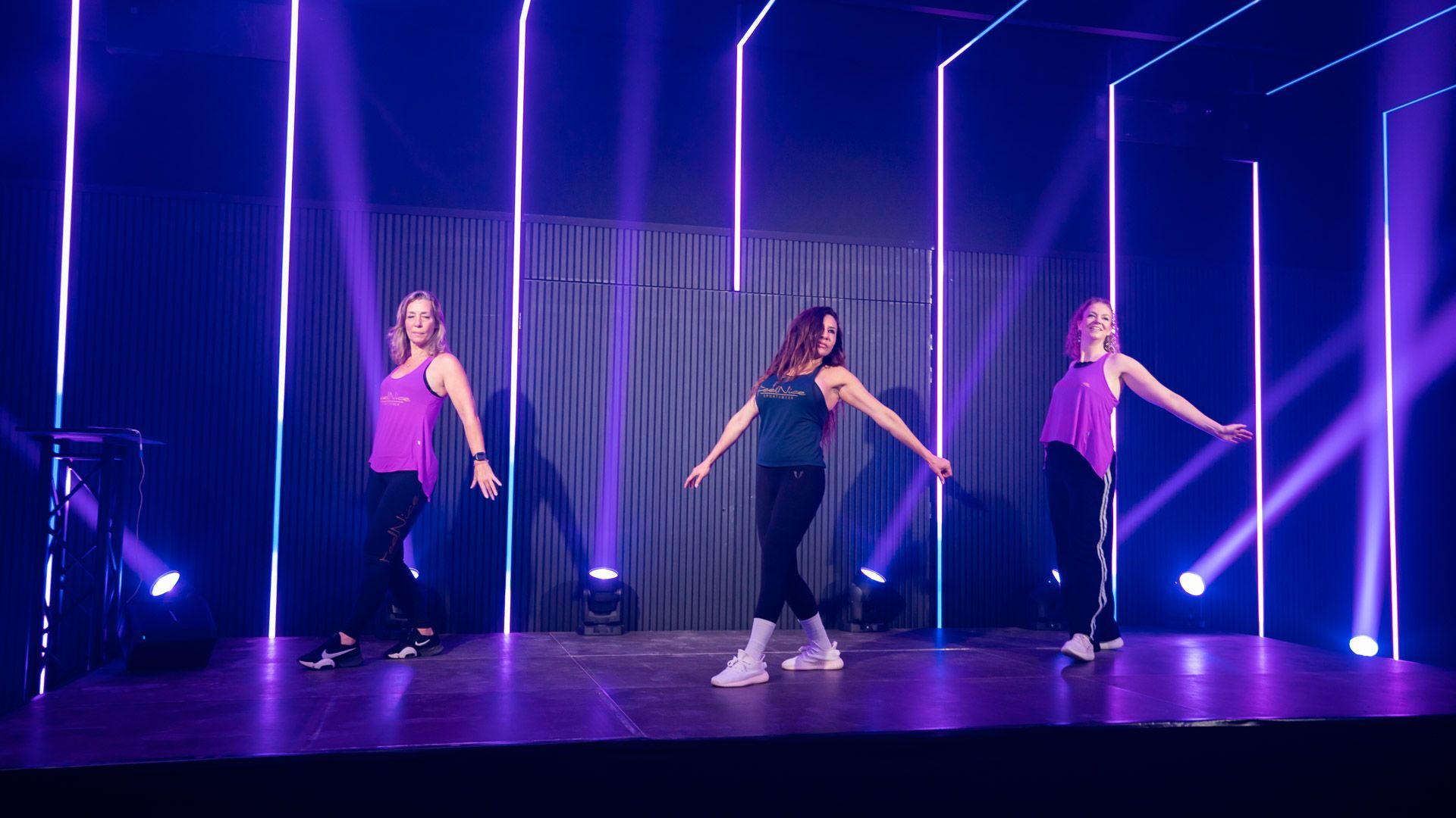 Vrouwen op yogamatten voeren een oefening uit voor het strekken van de vier poten van de heupen in een sportschool met grote ramen.
