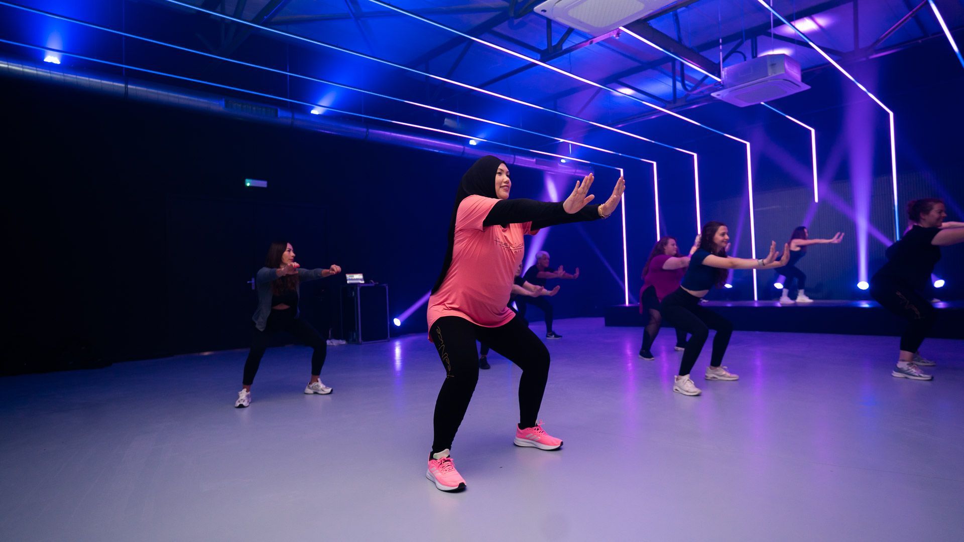 Vrouw in de sportschool, gebogen over dumbbell row op een bankje, draagt een rode legging en een wit topje.