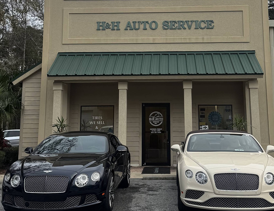 Two luxury cars parked outside The Auto Service shop with a green awning