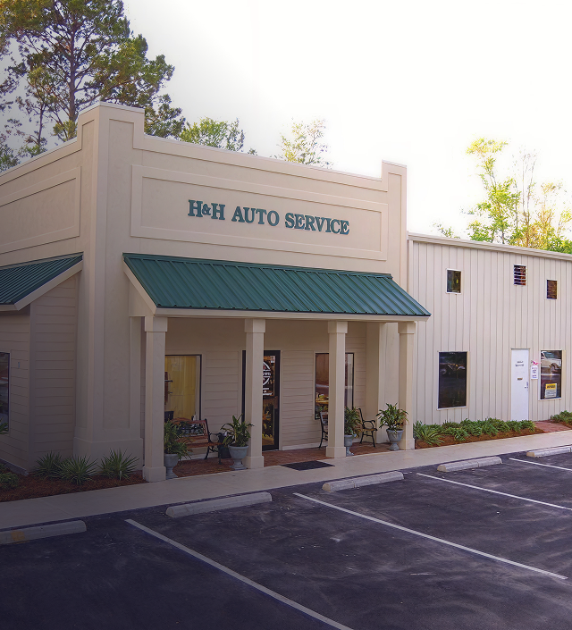 Front view of a beige auto service shop with a teal awning and empty parking lot