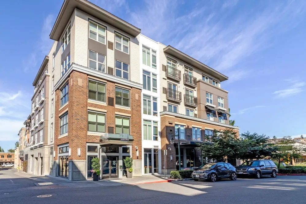 Modern apartment building with brick, light-colored siding, and parked cars in front.