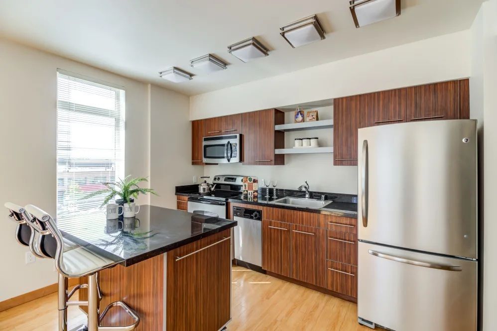 Modern kitchen with wood cabinets, stainless steel appliances, and a black countertop island.