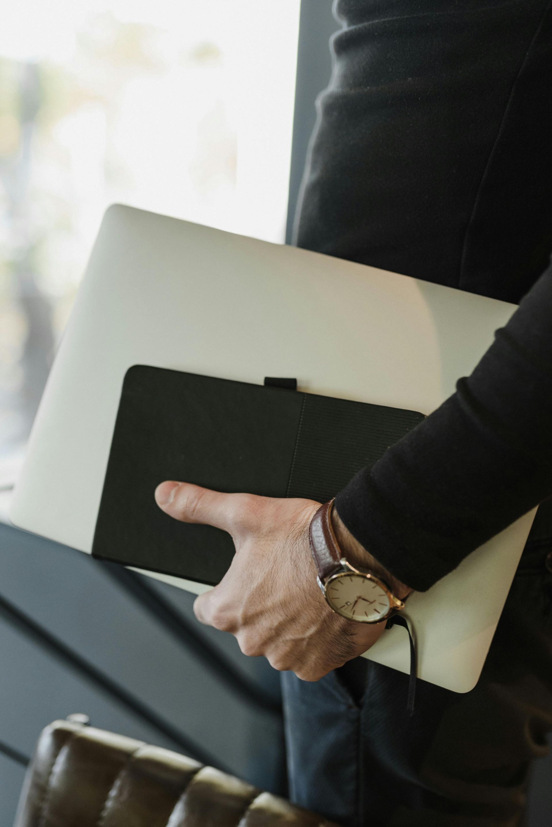 Person holding a laptop and a black tablet, wearing a watch.