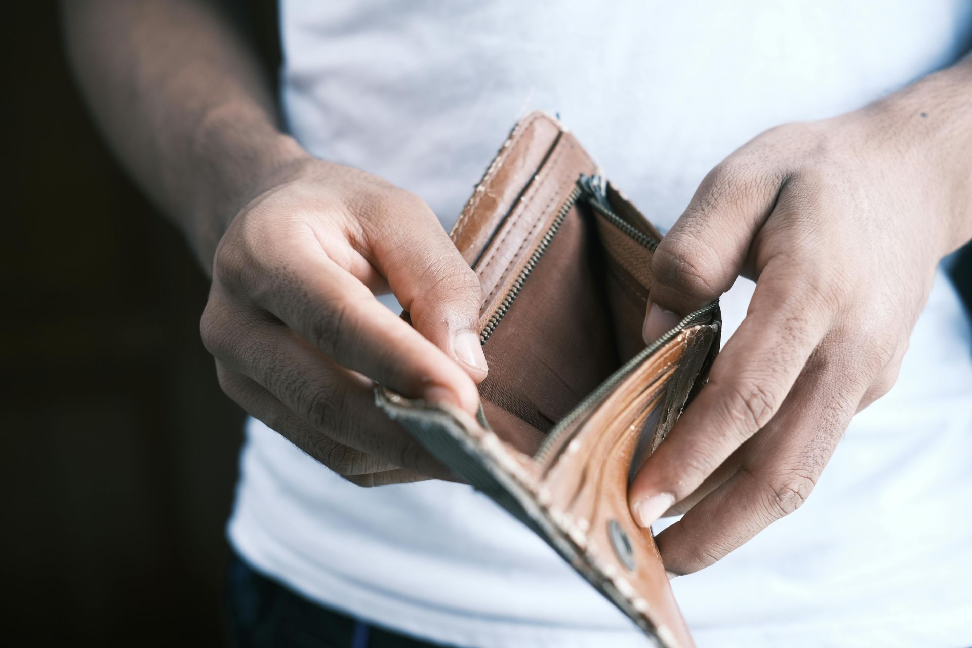 Hands holding an empty, open brown wallet, showing financial hardship.