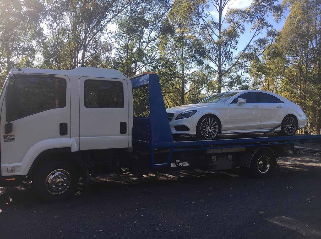 A Tow Truck is Carrying a White Car on the Back of It — Quick Hitch Towing & Tilt Tray Services Illawarra in Albion Park, NSW