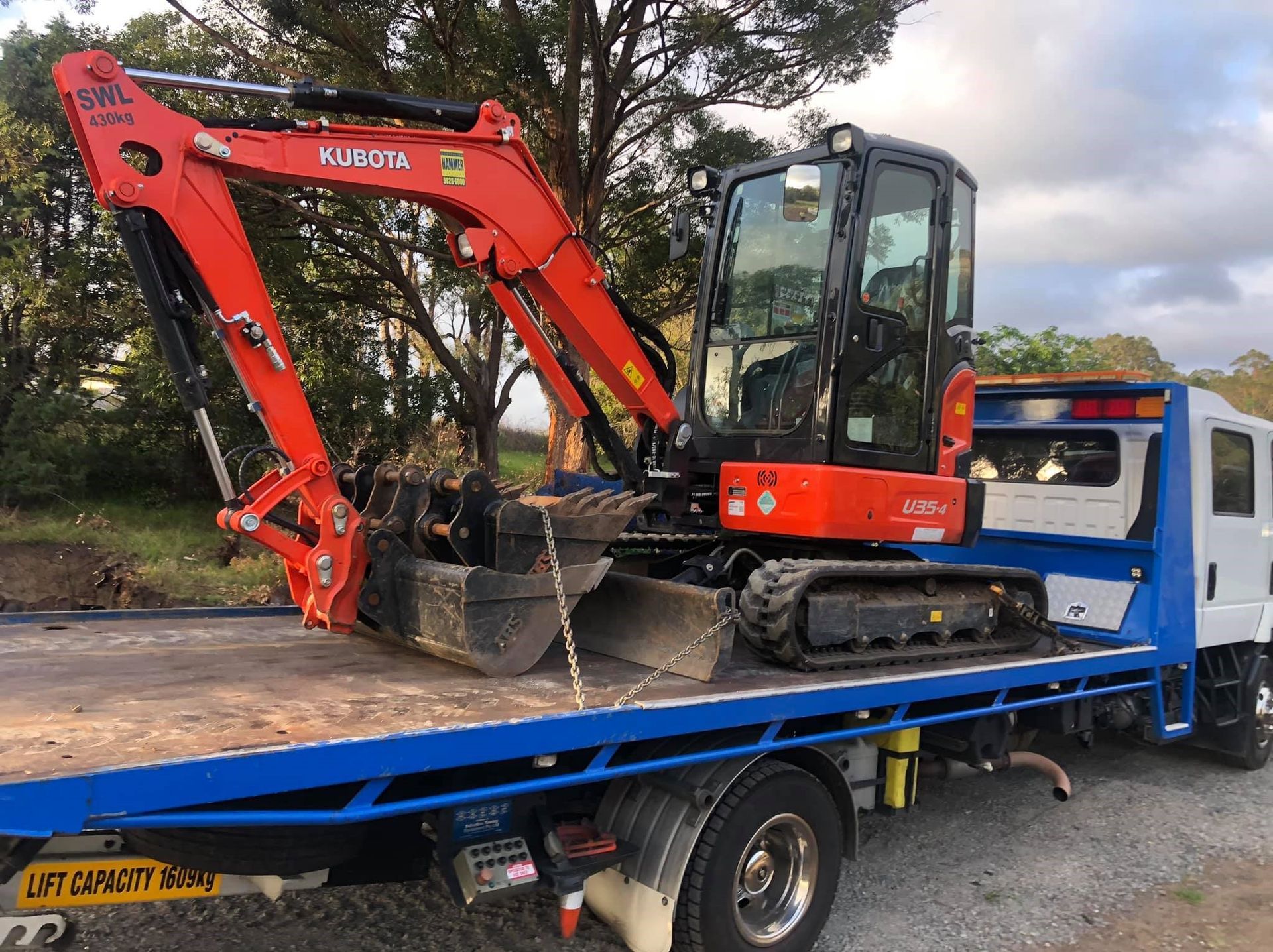 A Red Excavator is Sitting on Top of a Blue Tow Truck — Quick Hitch Towing & Tilt Tray Services Illawarra in Dapto, NSW