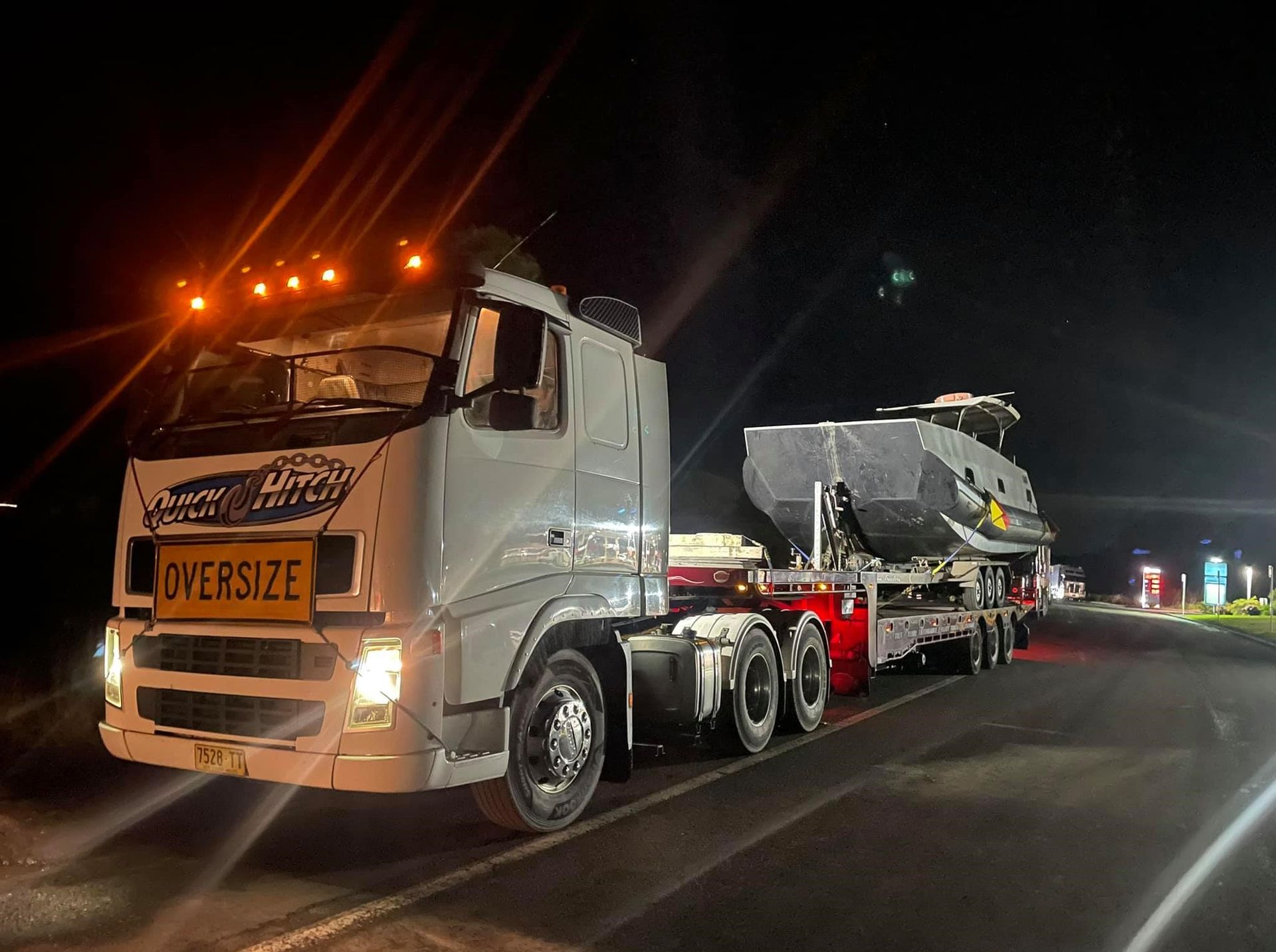 A Large Truck is Carrying a Boat Down a Road at Night — Quick Hitch Towing & Tilt Tray Services Illawarra in Dapto, NSW