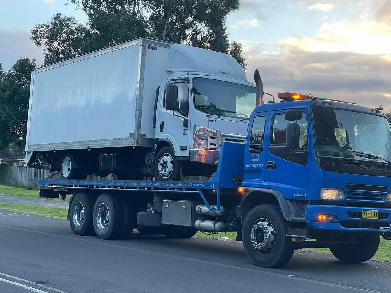 A Blue Tow Truck is Towing a White Truck Down the Road — Quick Hitch Towing & Tilt Tray Services Illawarra in Oak Flats, NSW