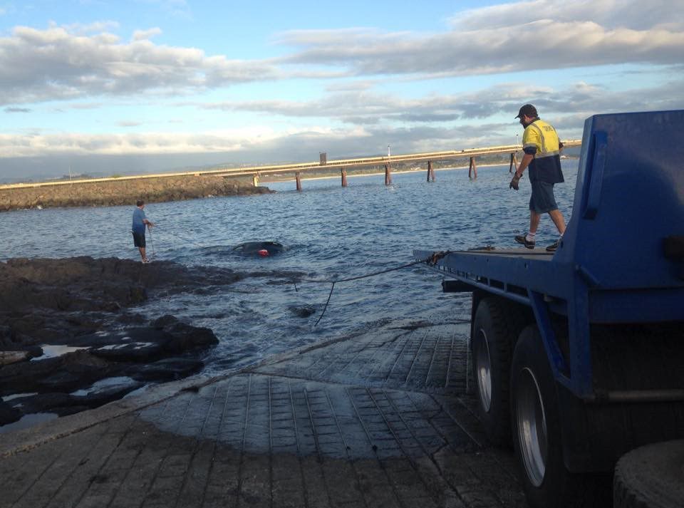 A Man is Standing on the Back of a Blue Truck — Quick Hitch Towing & Tilt Tray Services Illawarra in Albion Park, NSW