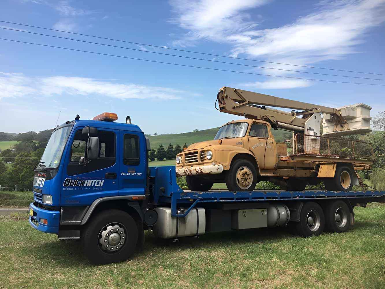 A Blue Tow Truck With a Truck on the Back is Parked — Quick Hitch Towing & Tilt Tray Services Illawarra in Port Kembla, NSW