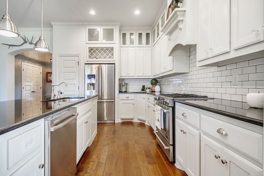 White kitchen with stainless steel appliances, dark countertops, and hardwood floors.