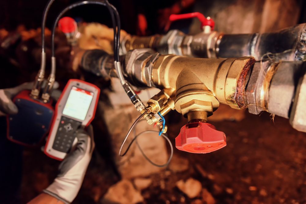 Hand holding a device connected to pipes with red knobs.