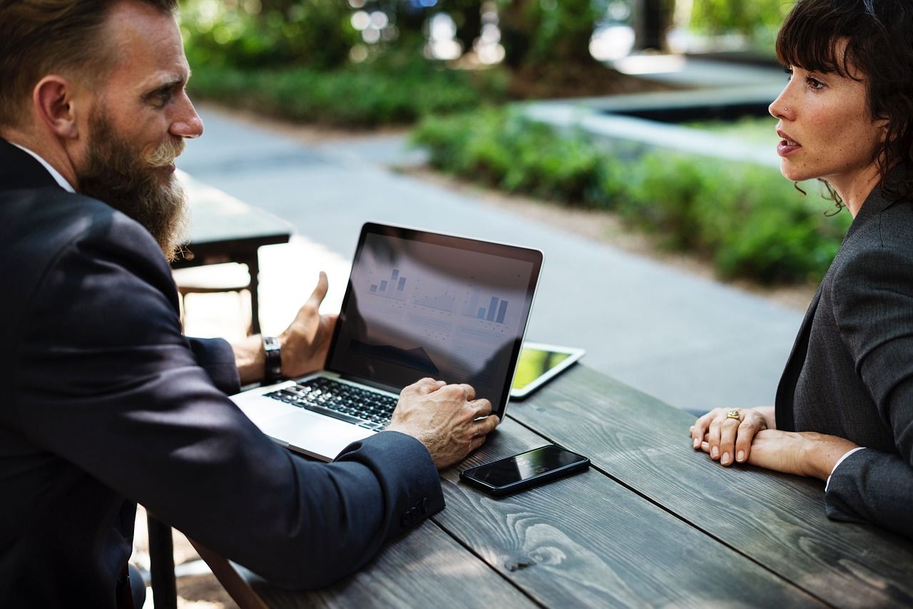 a man and a woman over a table, the man has a laptop in front of him