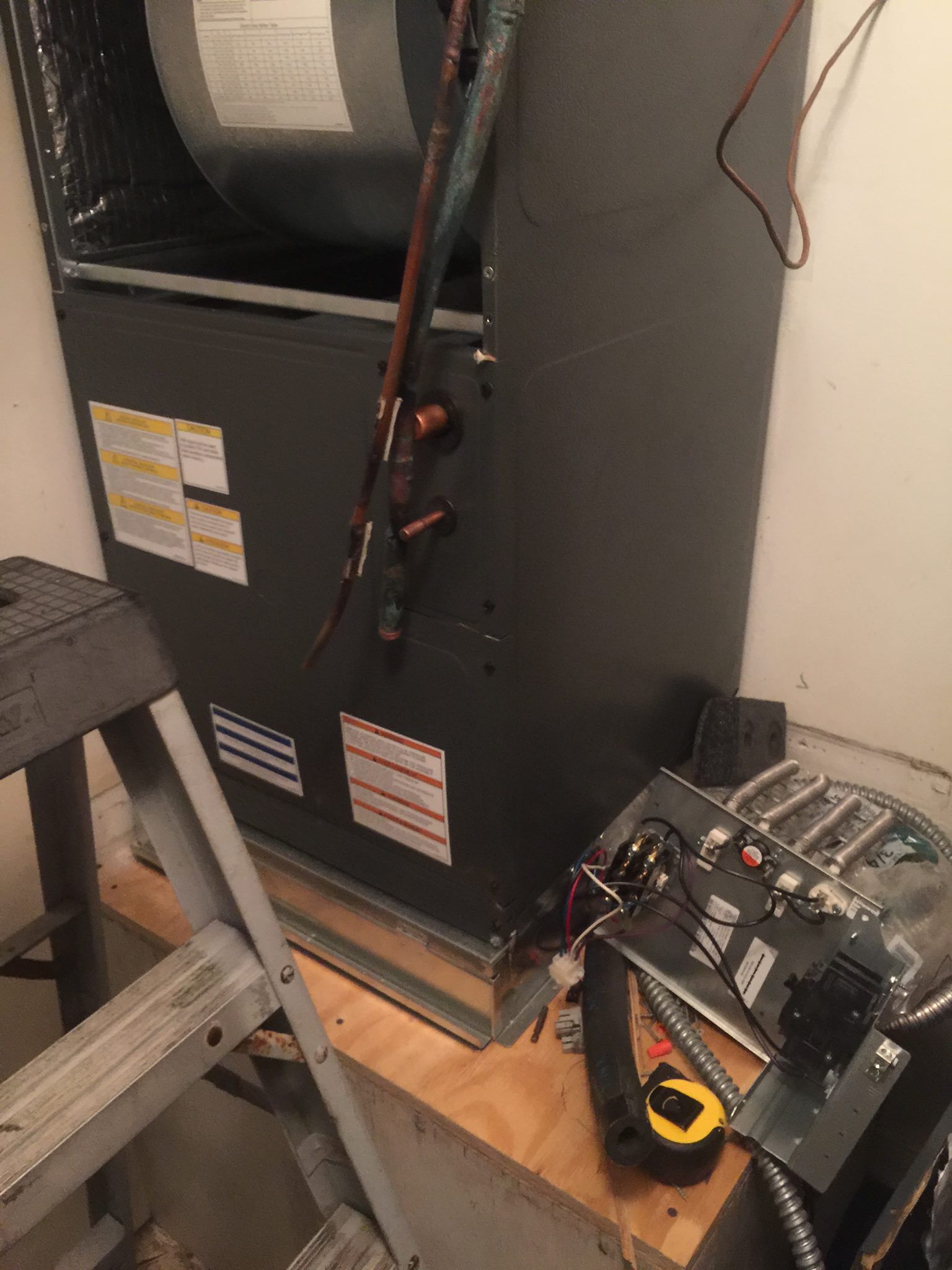 An air conditioner is sitting on a wooden table next to a ladder.