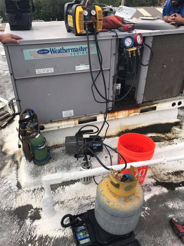 A man is working on an air conditioner on a roof.