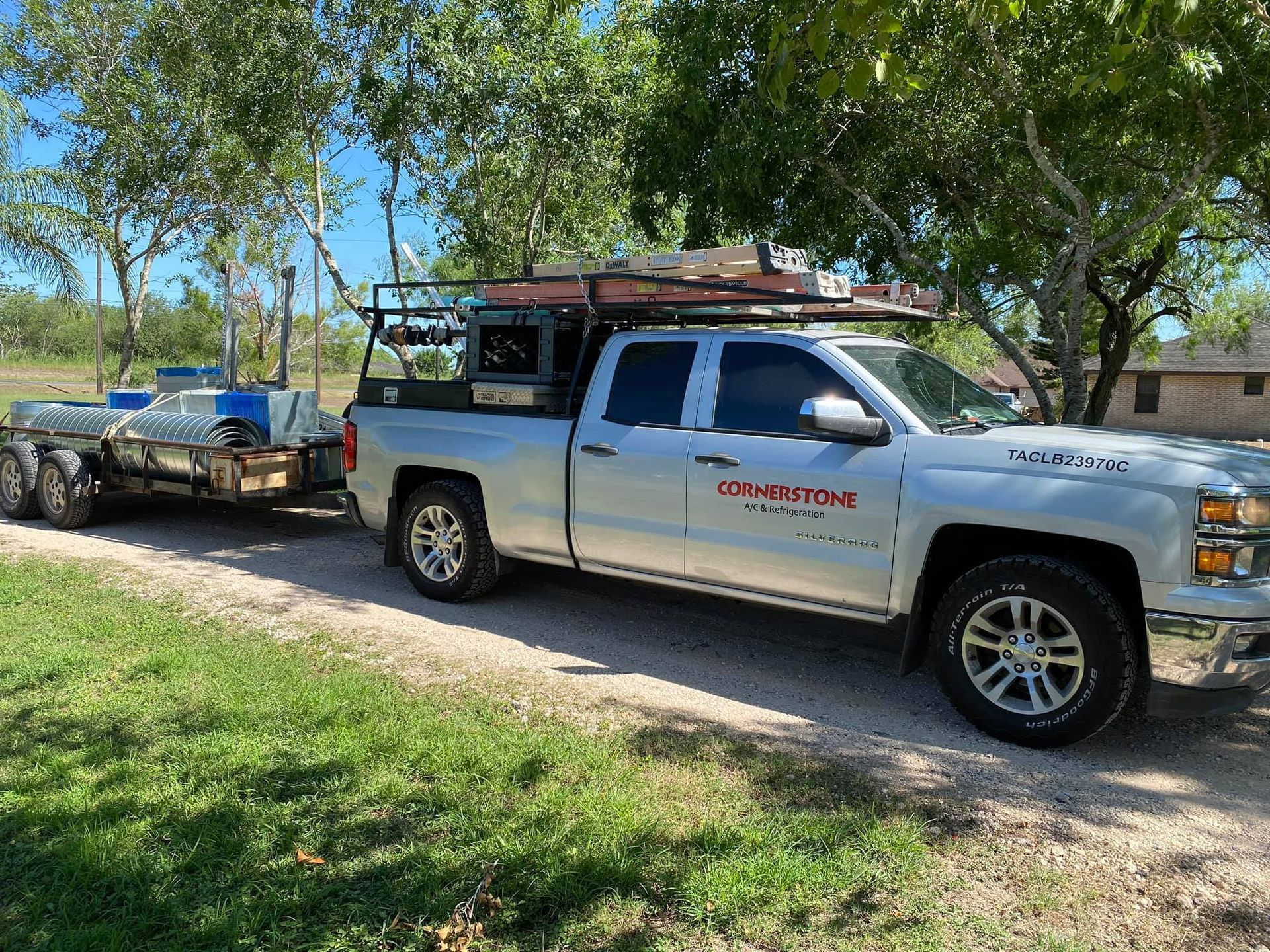 A silver truck with a trailer attached to it is parked on a dirt road.