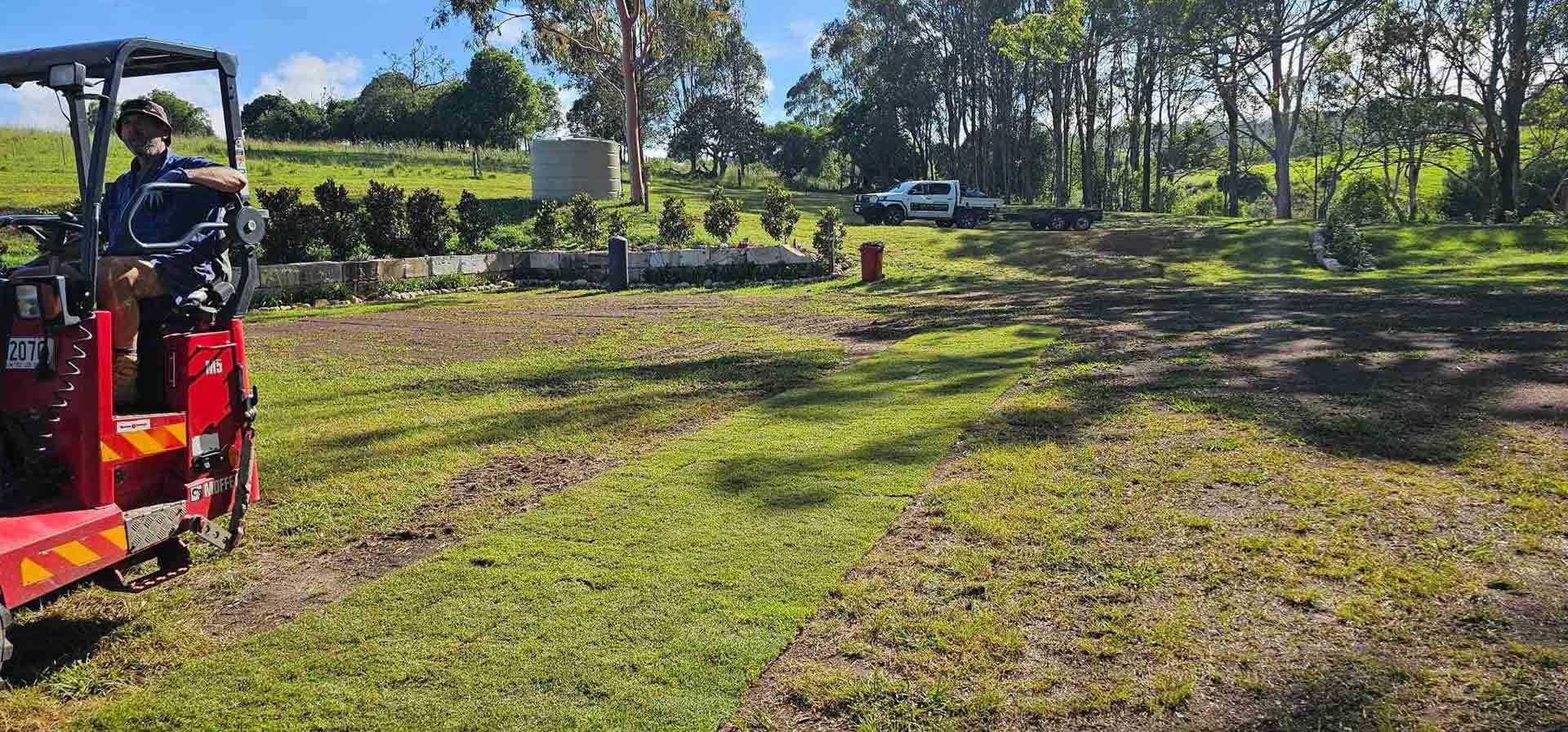 A Man Is Driving A Small Red Tractor Through A Grassy Field — Joe's Turf In Spring Creek, QLD