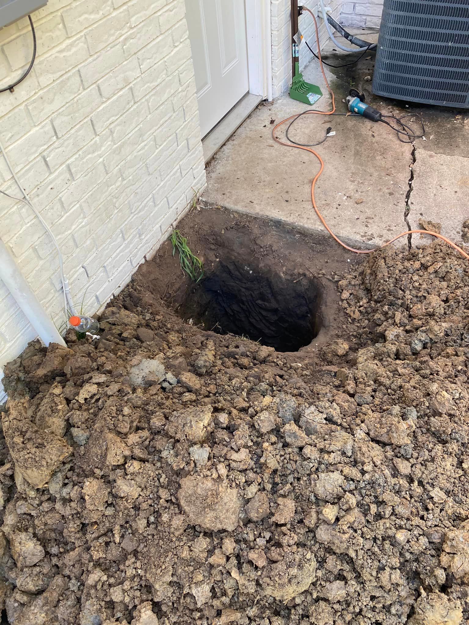 A hole in the ground next to a brick wall.