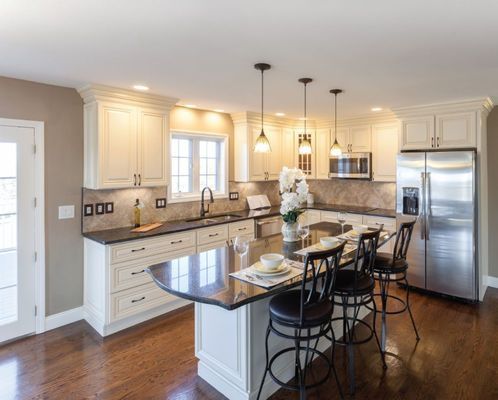 A kitchen with white cabinets , black counter tops , stainless steel appliances and a large island.