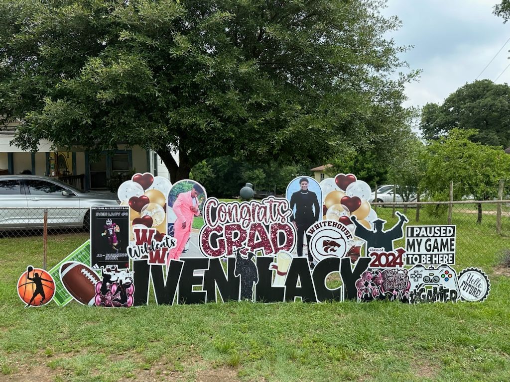 A graduation sign is sitting in the grass in front of a house.