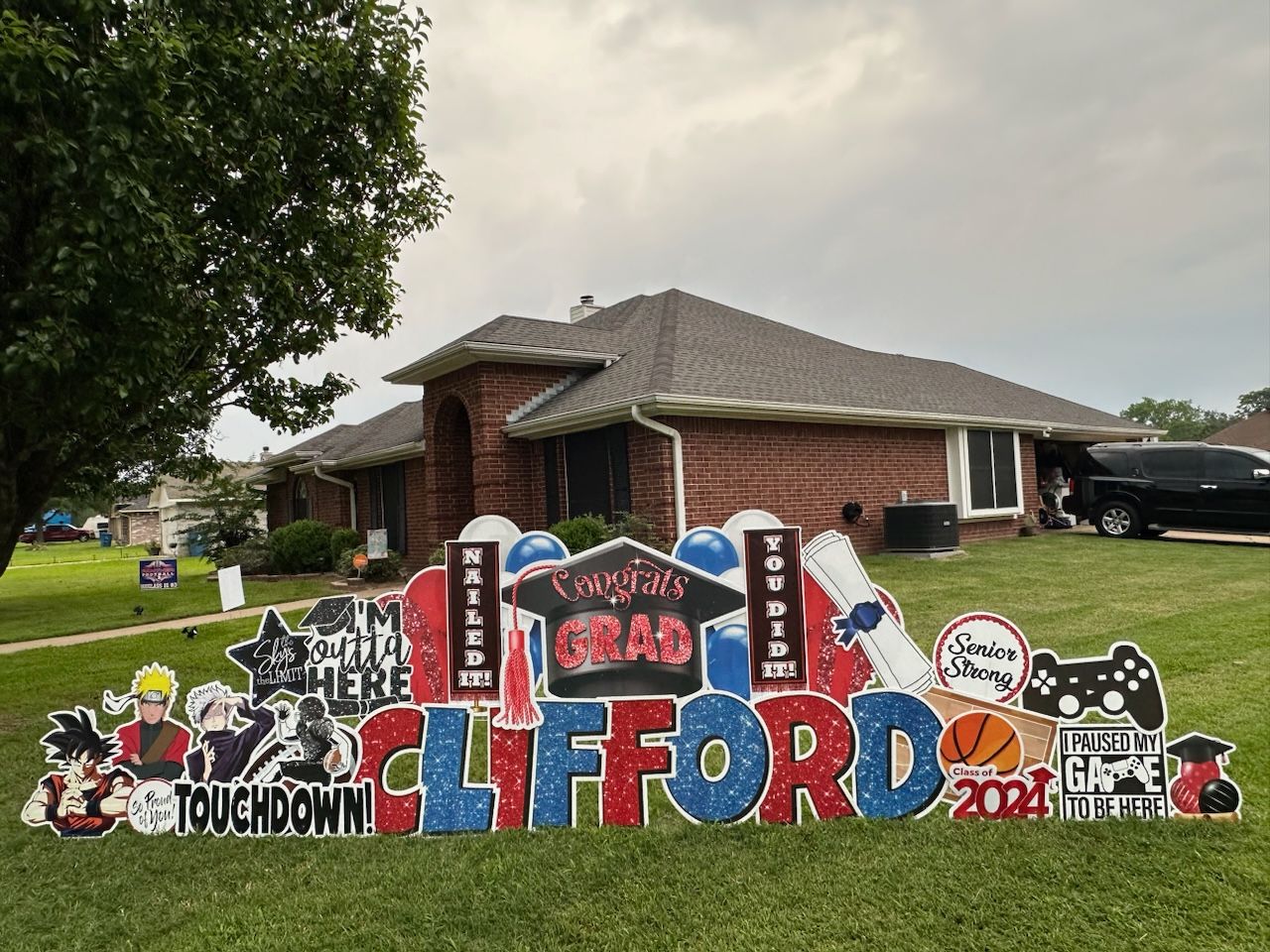A yard sign for a graduate is in front of a brick house.