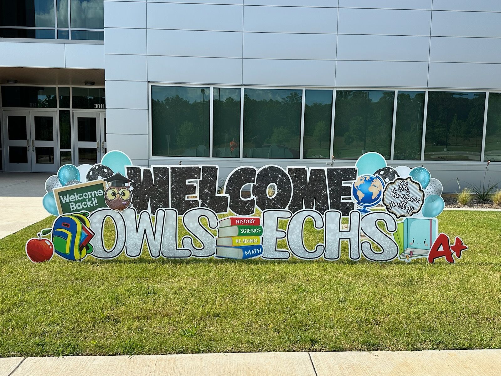 A welcome sign is sitting in front of a school building.