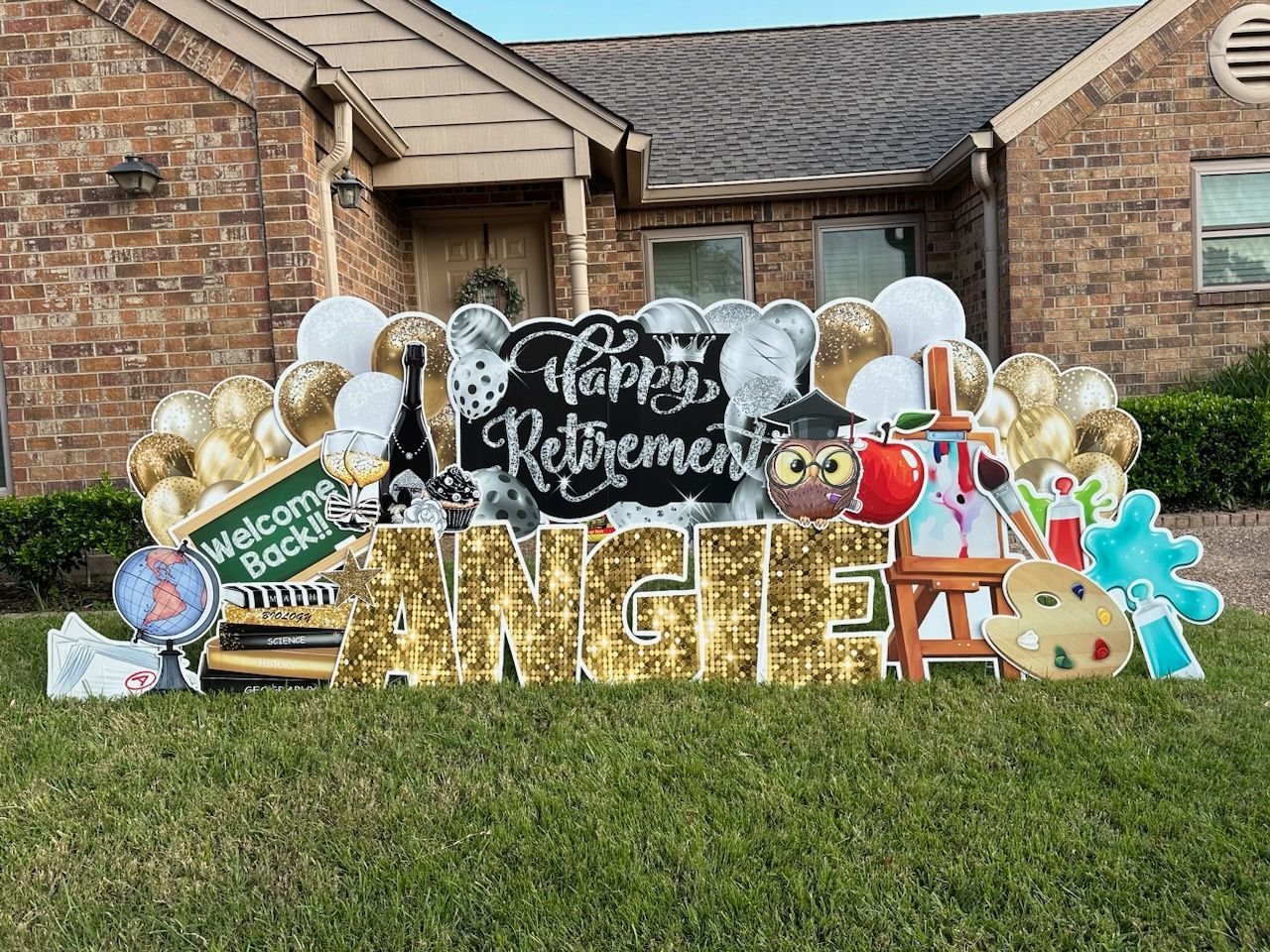 A large yard sign for a retirement party is in front of a brick house.