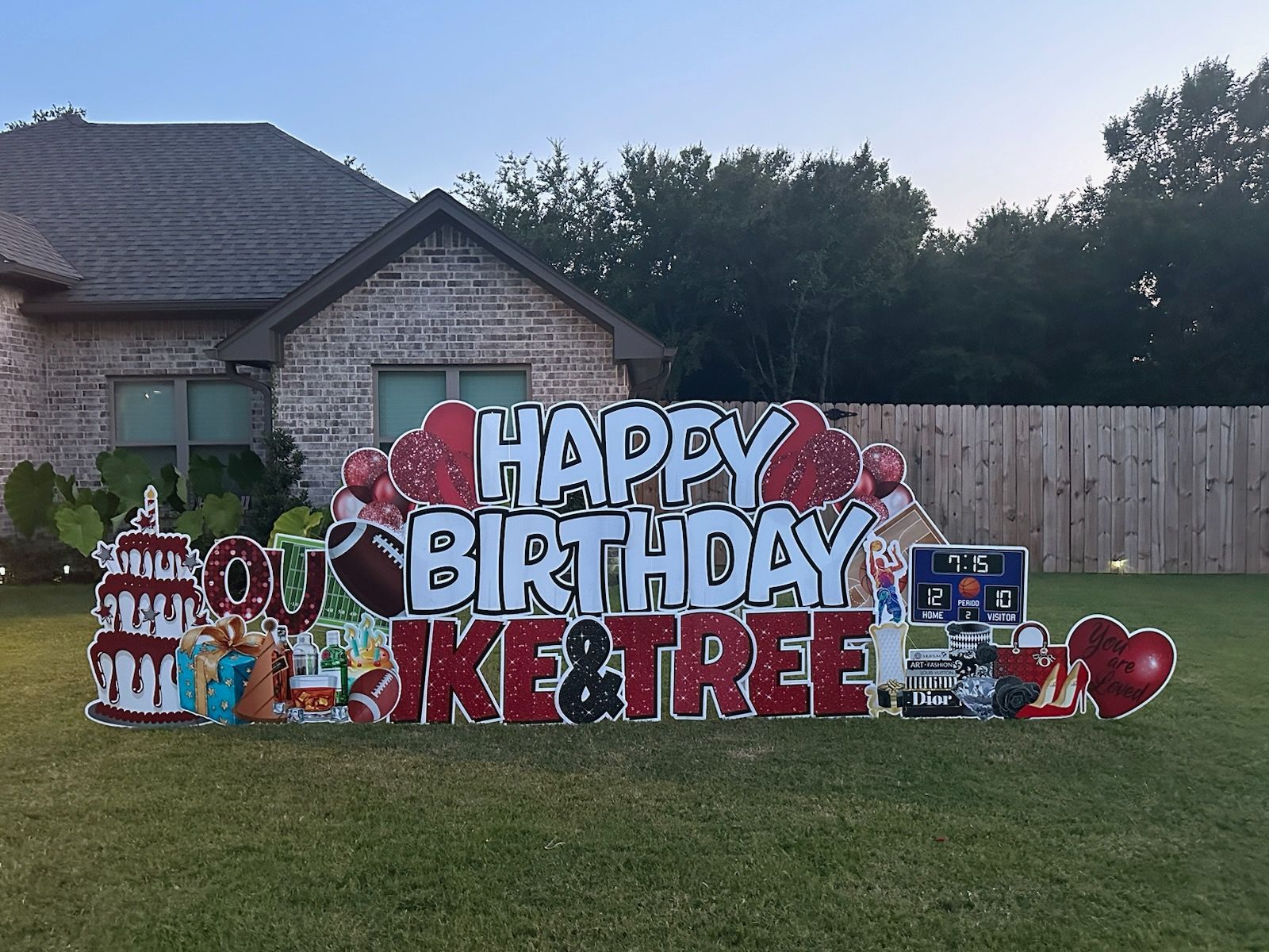 A large happy birthday sign is in front of a brick house.