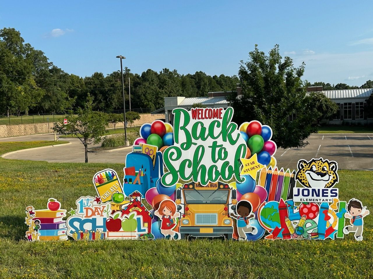 A back to school sign is sitting in the grass in front of a school.