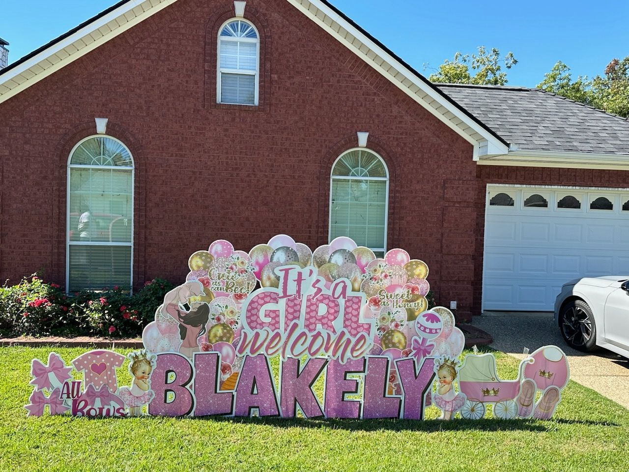 A welcome sign for a baby girl is in front of a brick house.
