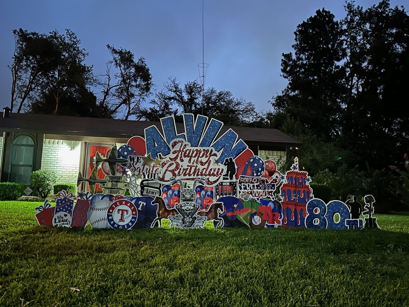 A happy birthday sign is sitting in the grass in front of a house.