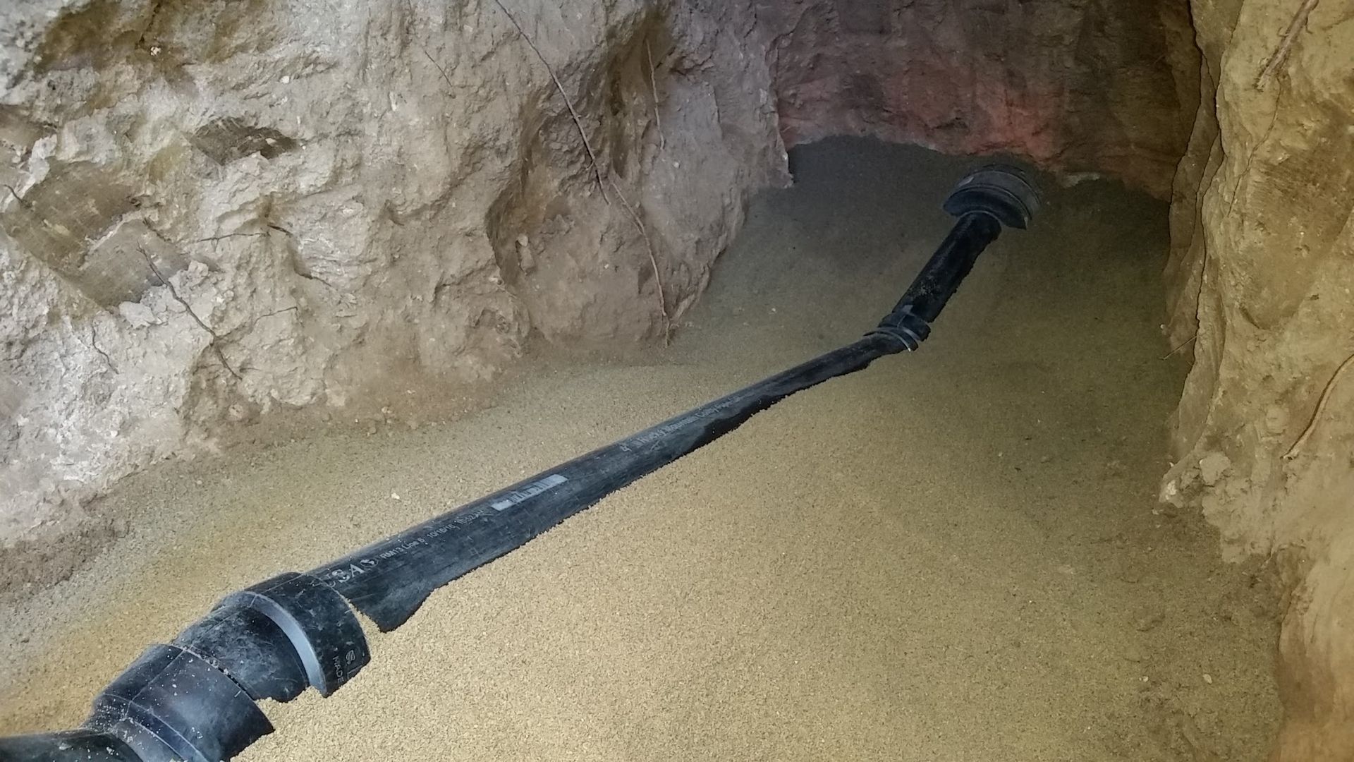 Black pipe extends into a sand-covered cave, likely for drainage or irrigation.
