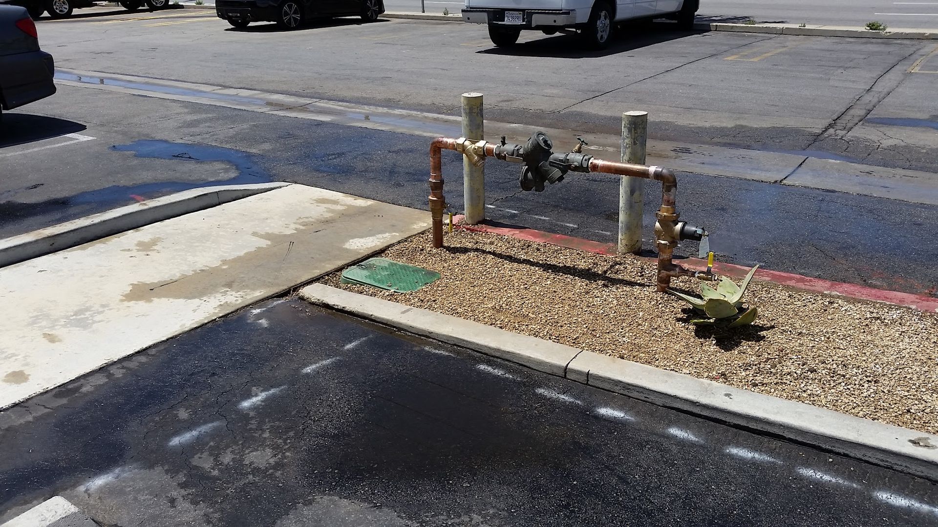 Water valve and pipes in a gravel bed in a parking lot, water on the asphalt.