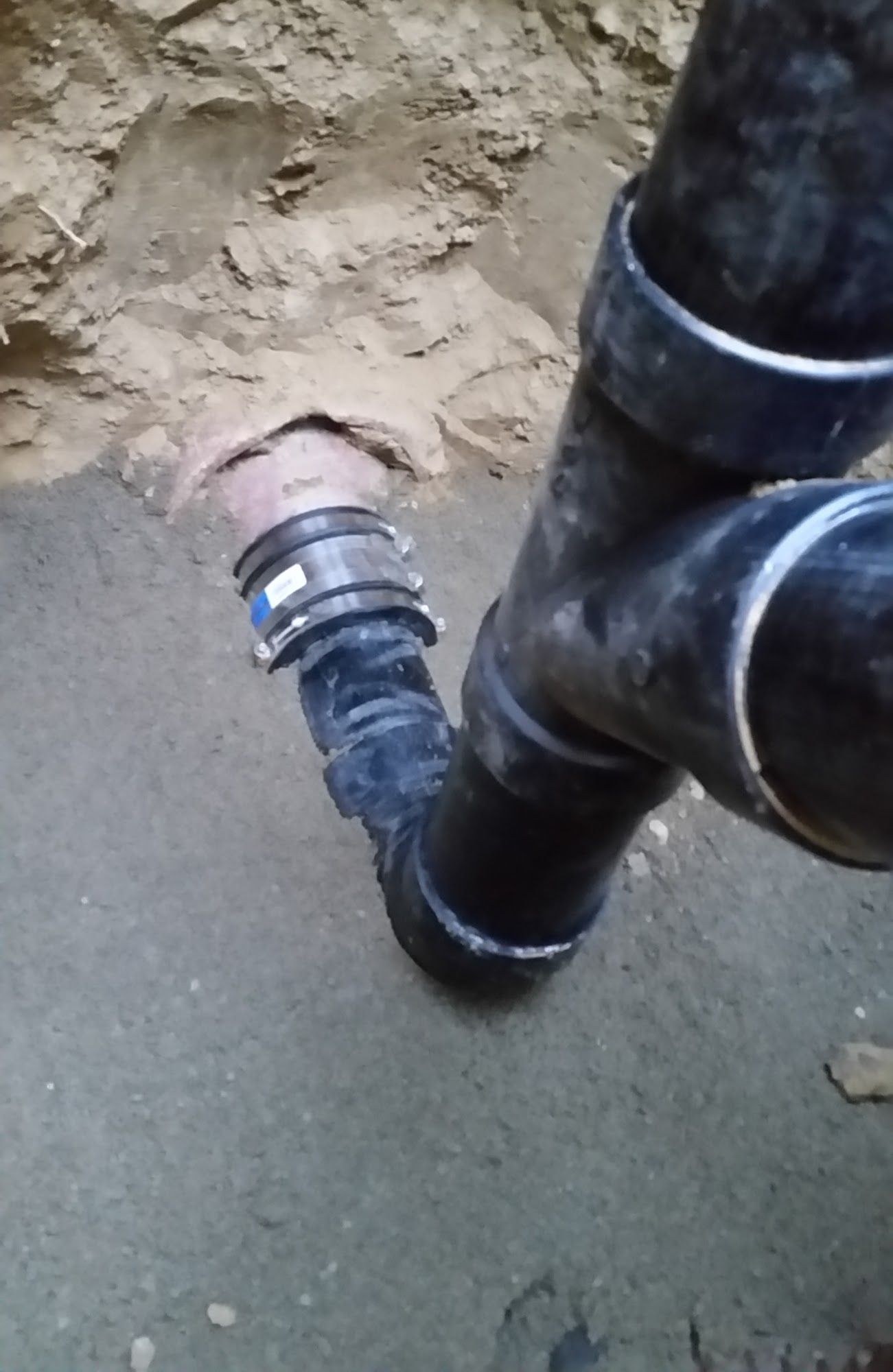 Black PVC plumbing pipes and fitting in a dirt trench.