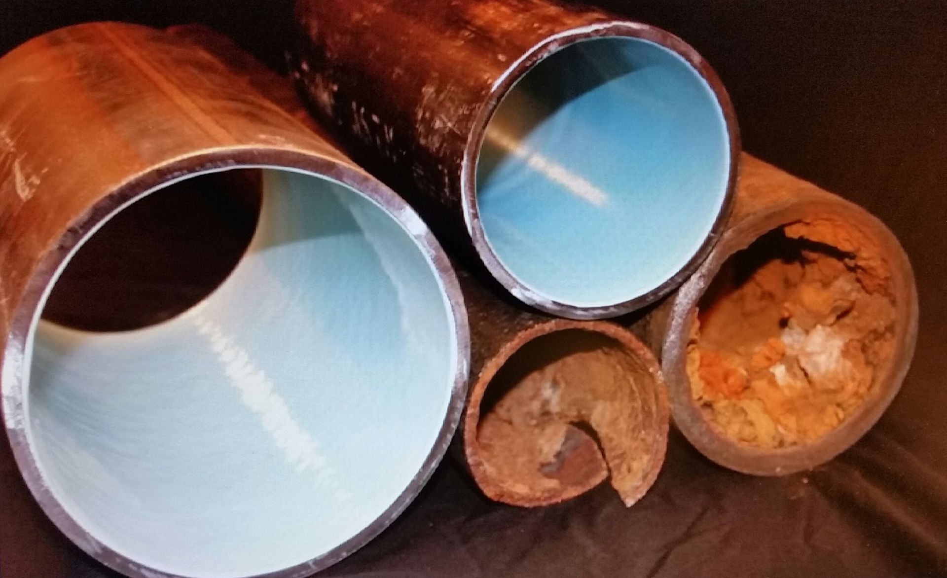 Cut-open rusty pipes with visible corrosion and buildup compared to coated, clean pipes.