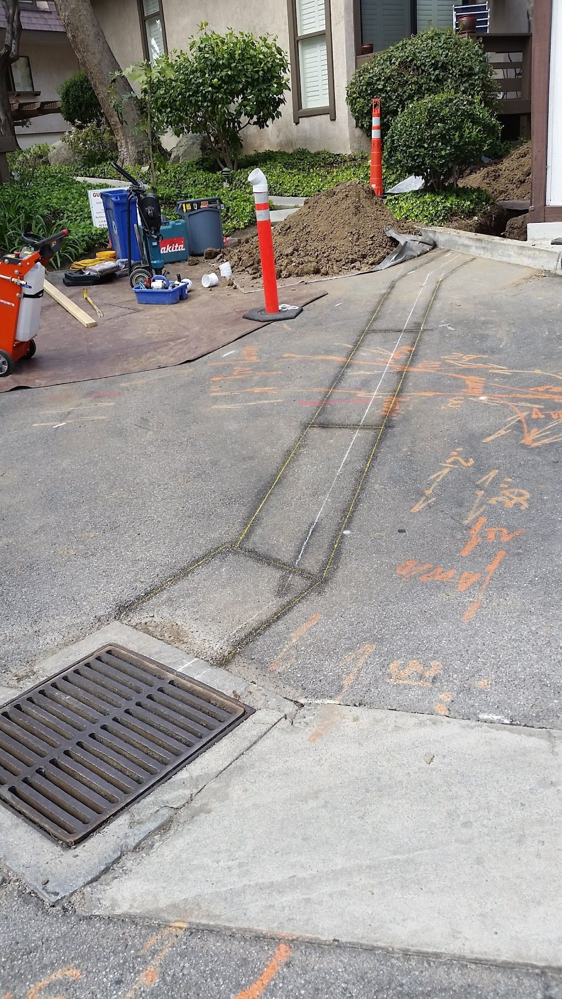 Asphalt driveway with a drainage grate. Lines and equipment suggest utility work.