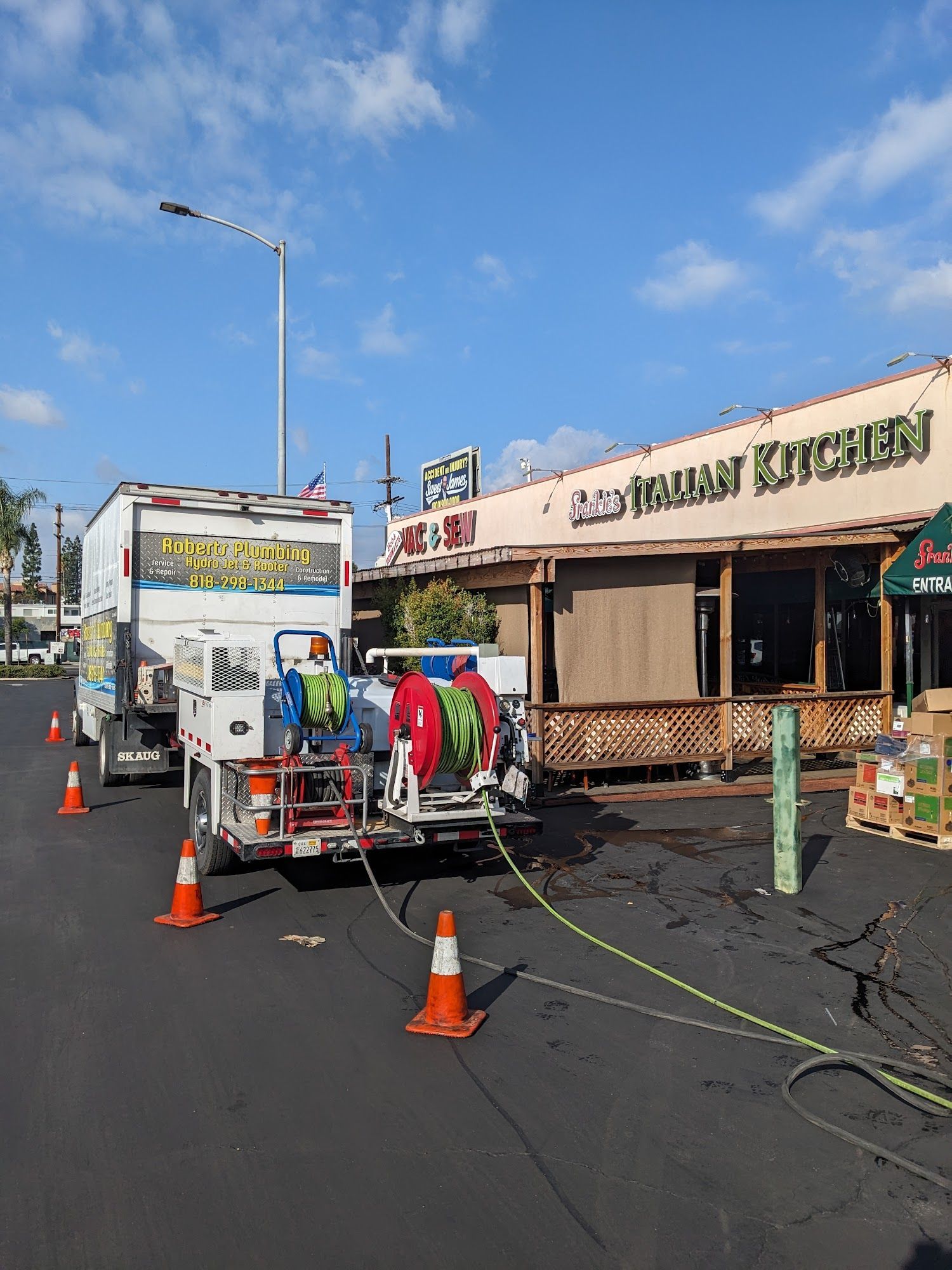 A water truck parked near a restaurant, connected by hoses. Orange cones line the street.
