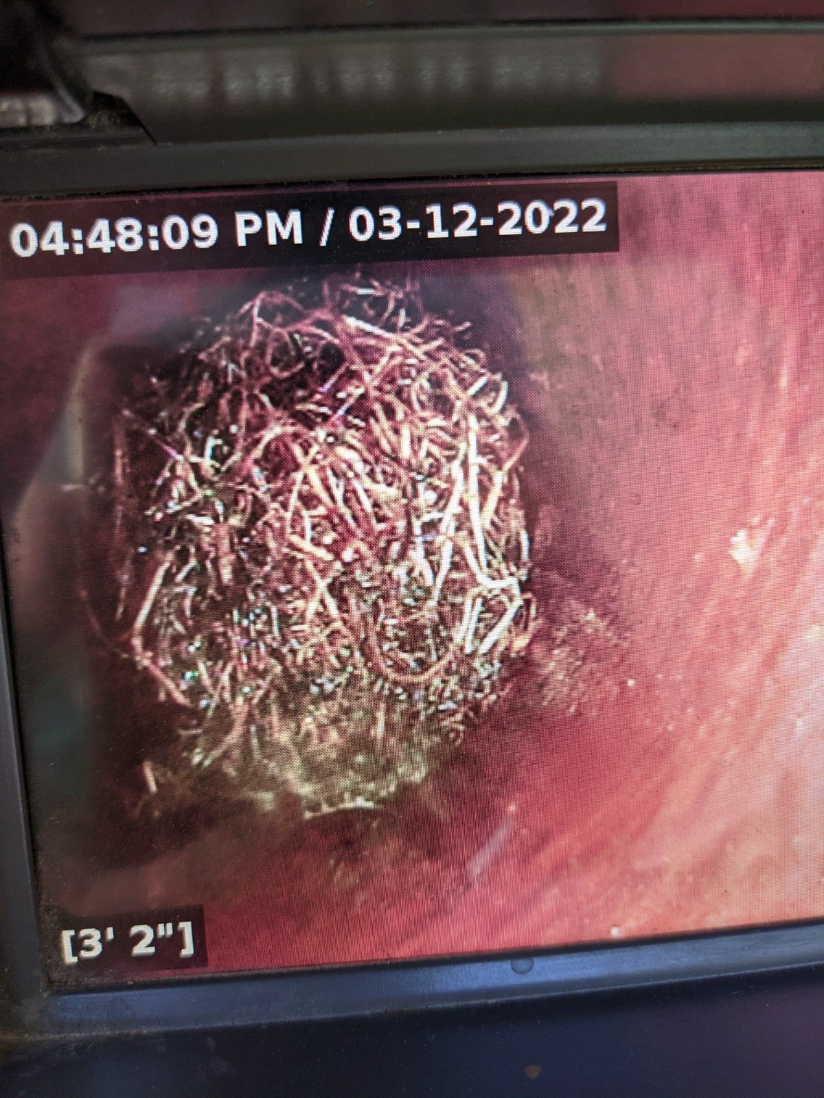 Camera view inside a pipe showing a large, tangled mass of copper wire.