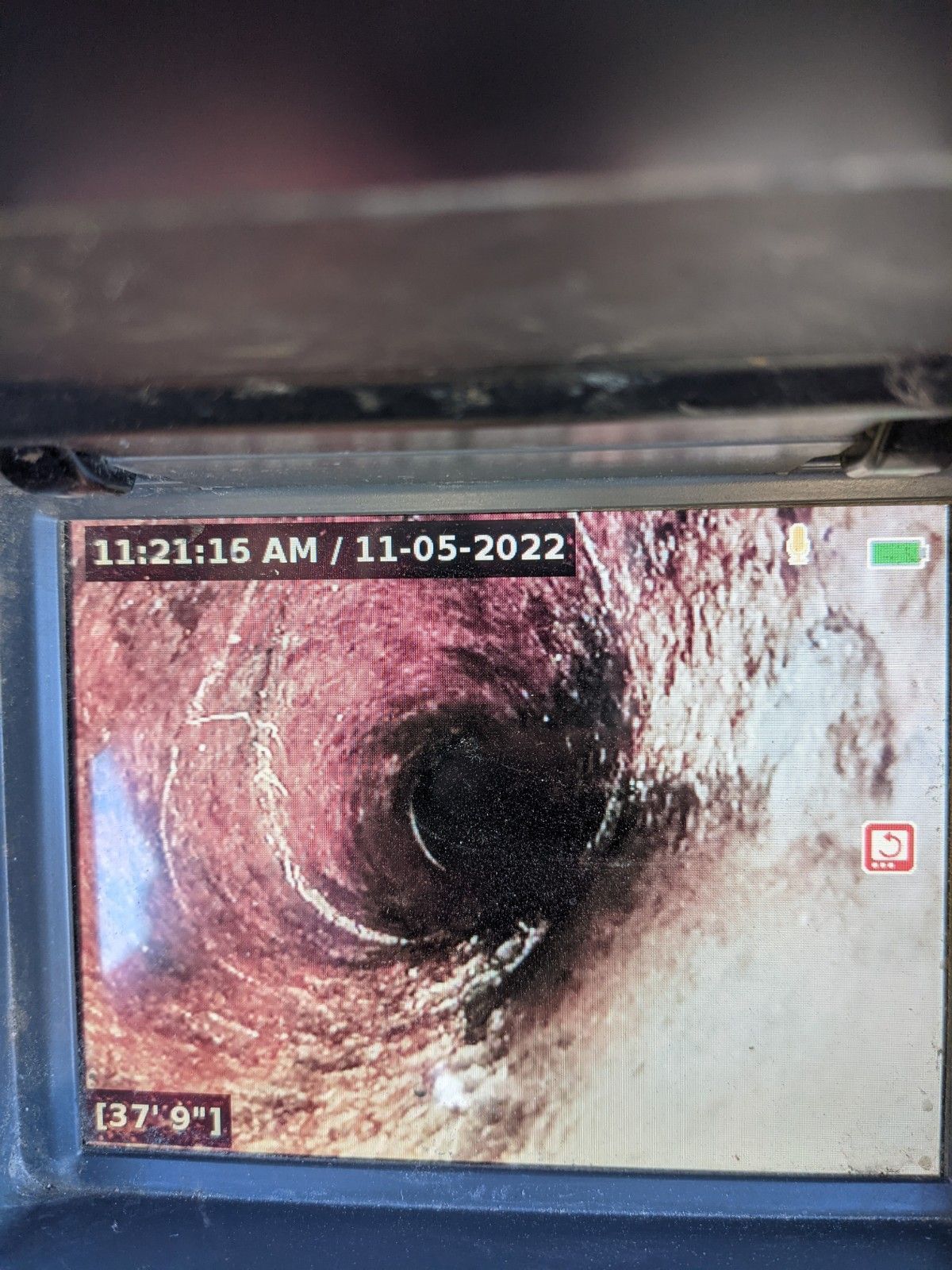 Inside a pipe, video screen showing dark interior with some white deposits. Date and time stamp in upper left.