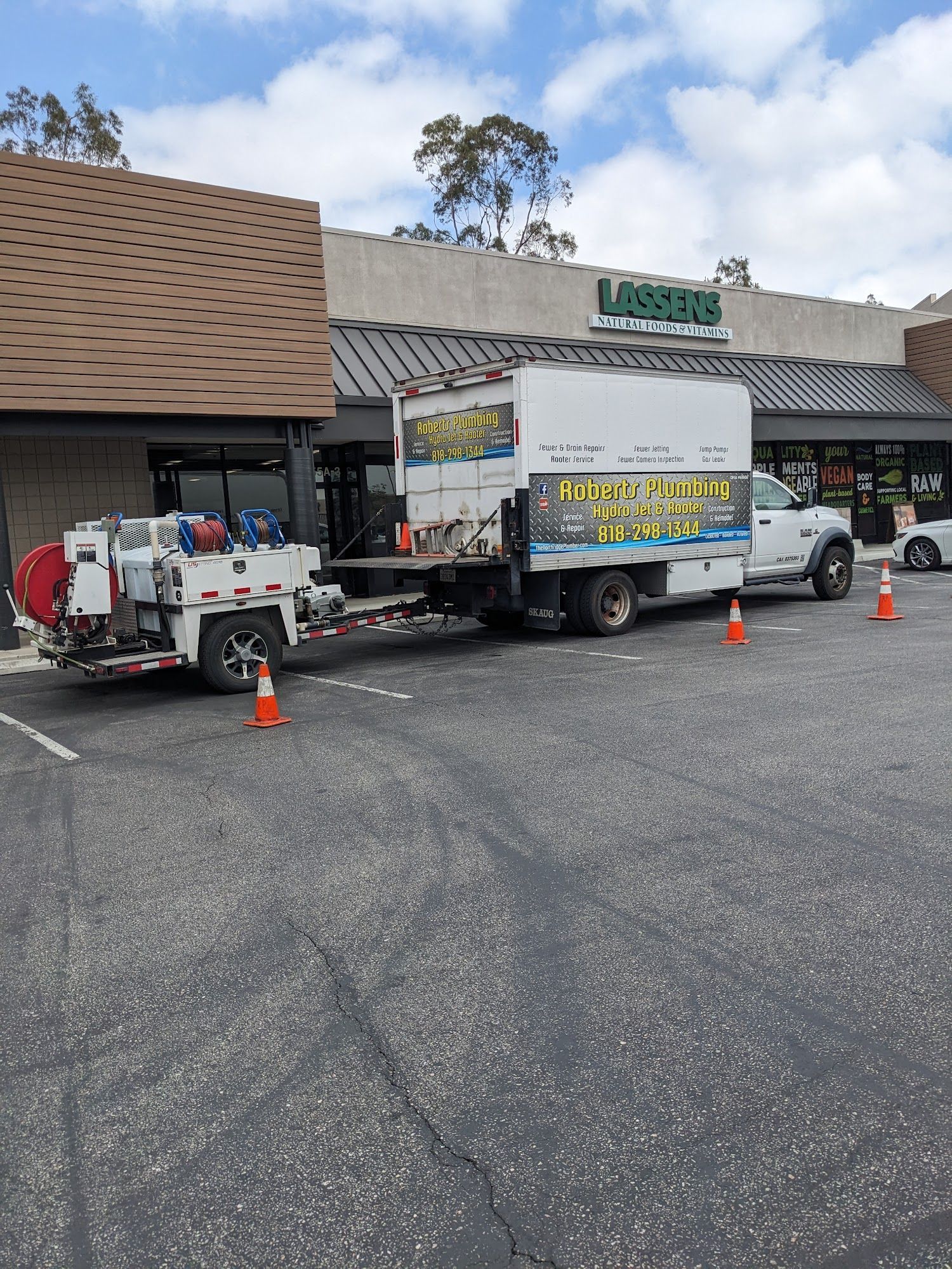 A work truck with a trailer parked in front of a store. Orange cones in parking lot.